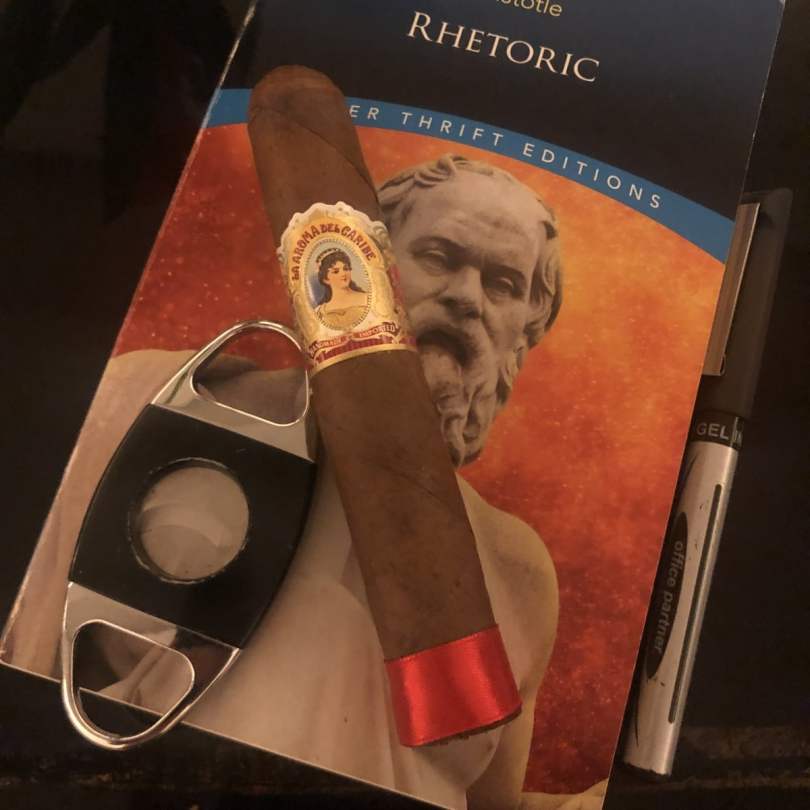 Smoking a cigar while reading philosophy. The Cigar is La Aroma Del Cariba Base Line Immensa. The book is Aristotle's Rhetoric.